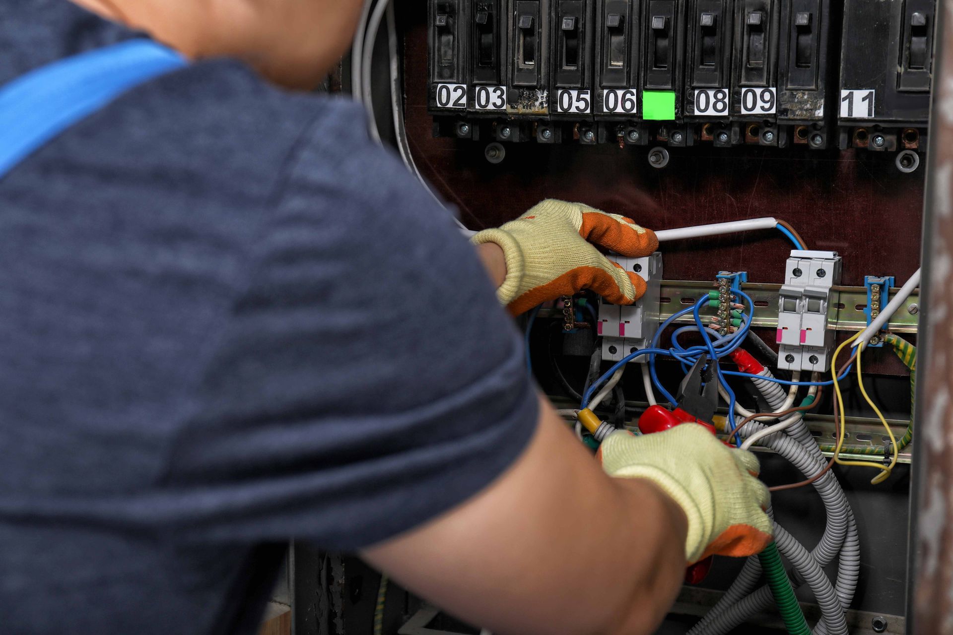 Hands using a digital multimeter to test wiring on an electrical panel