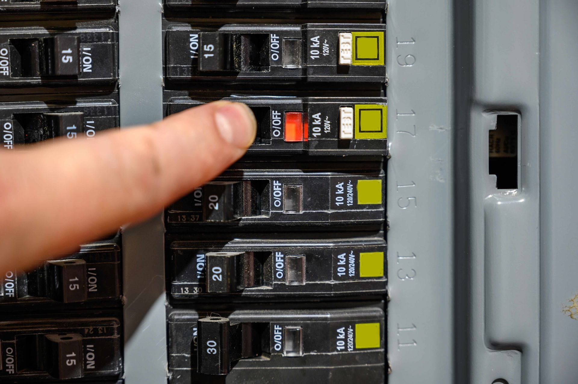 Finger pressing a red switch on an electrical breaker panel with black and yellow breakers