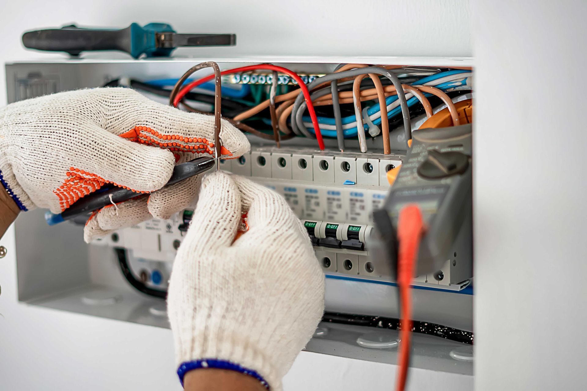 Gloved hands wiring an electrical breaker panel with orange and blue cables.