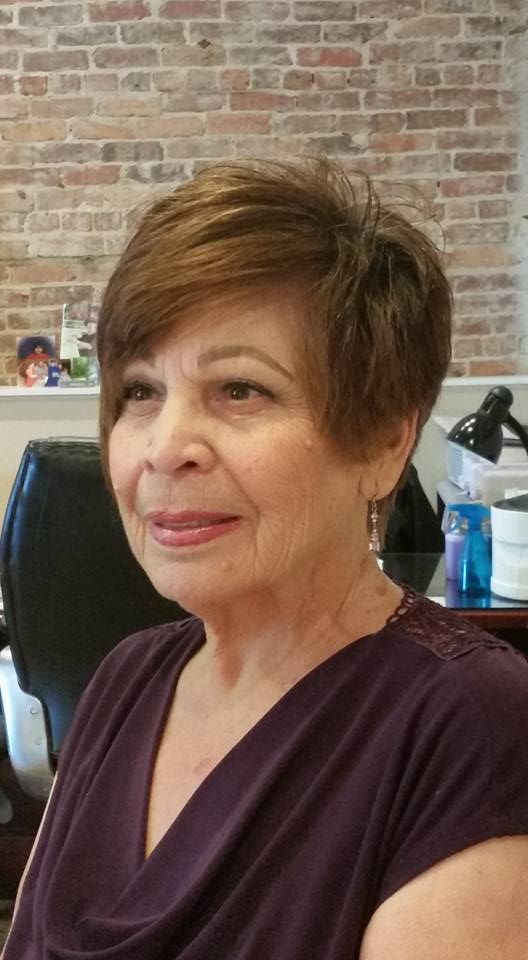 A woman in a purple shirt is sitting in front of a brick wall.