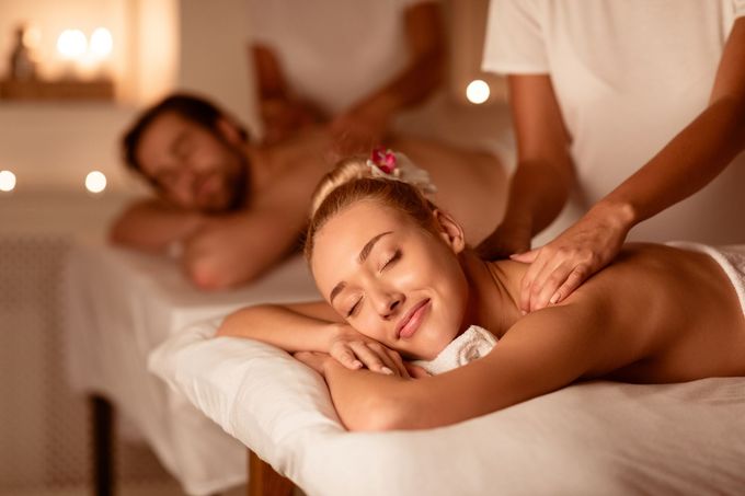 Couple Relaxing Receiving Back Massage Lying Closing Eyes At Romantic Luxury Spa With Burning Candles And Flowers. Wellness And Body Relaxation Therapy. Selective Focus, Low Light.