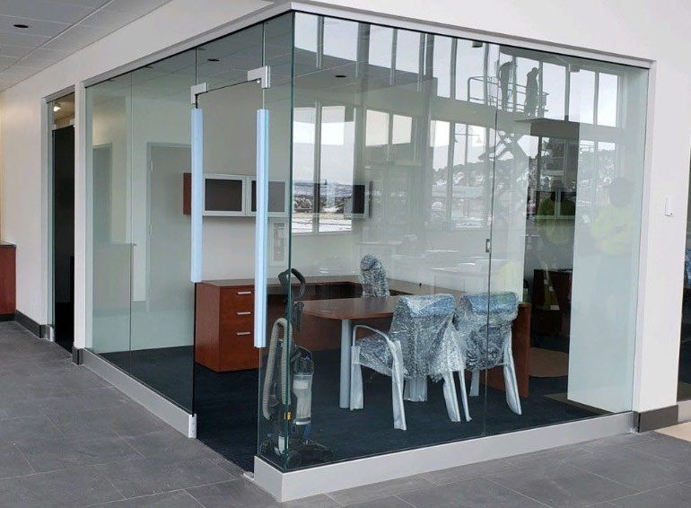 a room with a table and chairs behind a glass wall installed by Sun Glass