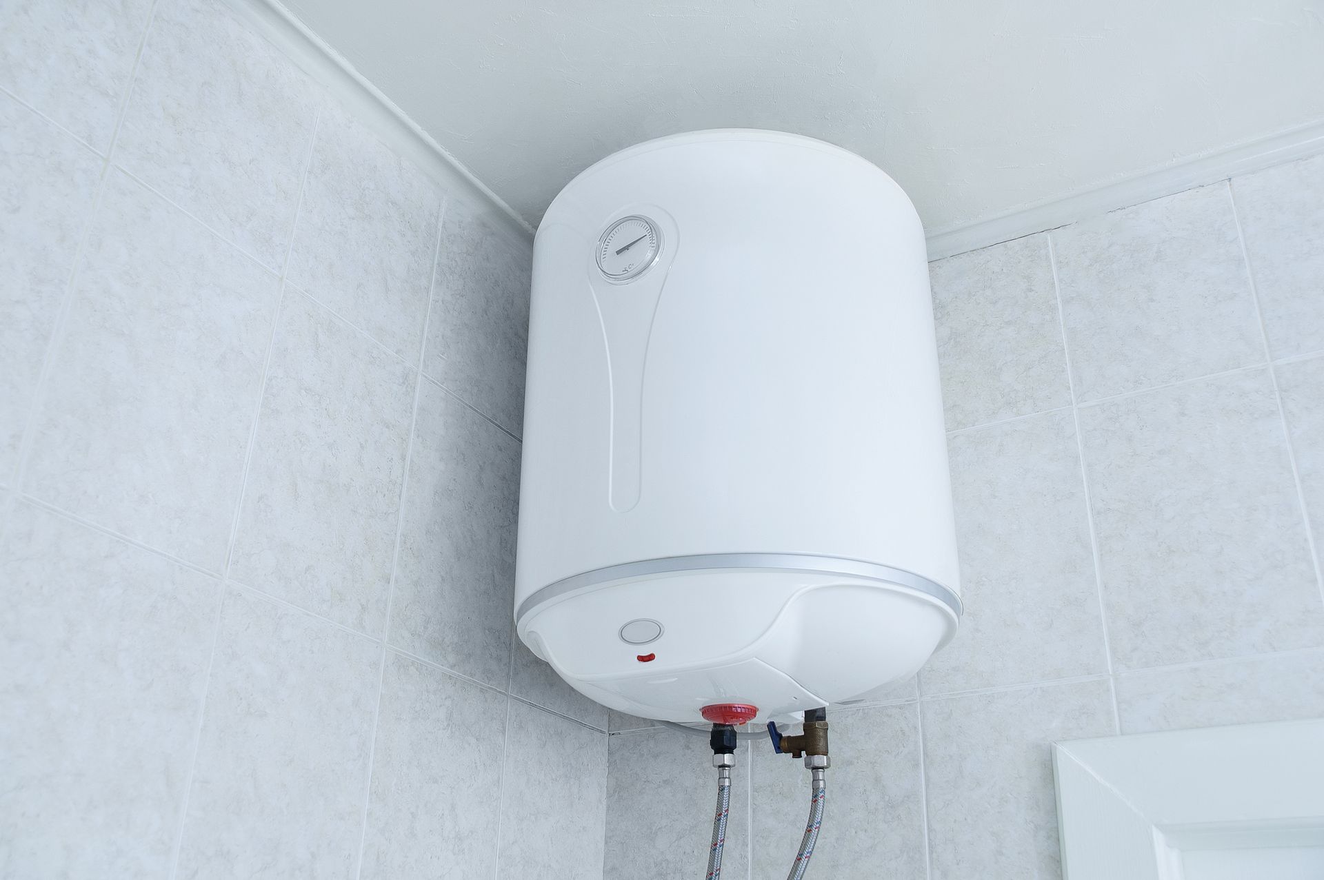 A white water heater is hanging from the ceiling in a bathroom.