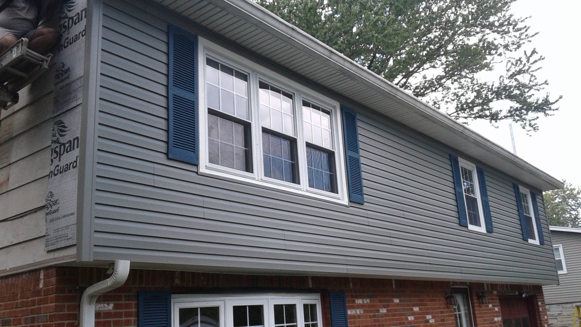 A house with a gray siding and blue shutters is being remodeled.