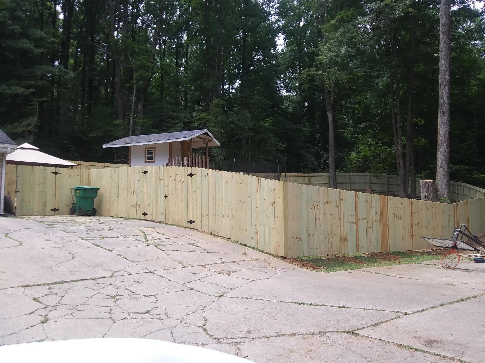 A wooden fence surrounds a driveway in front of a house