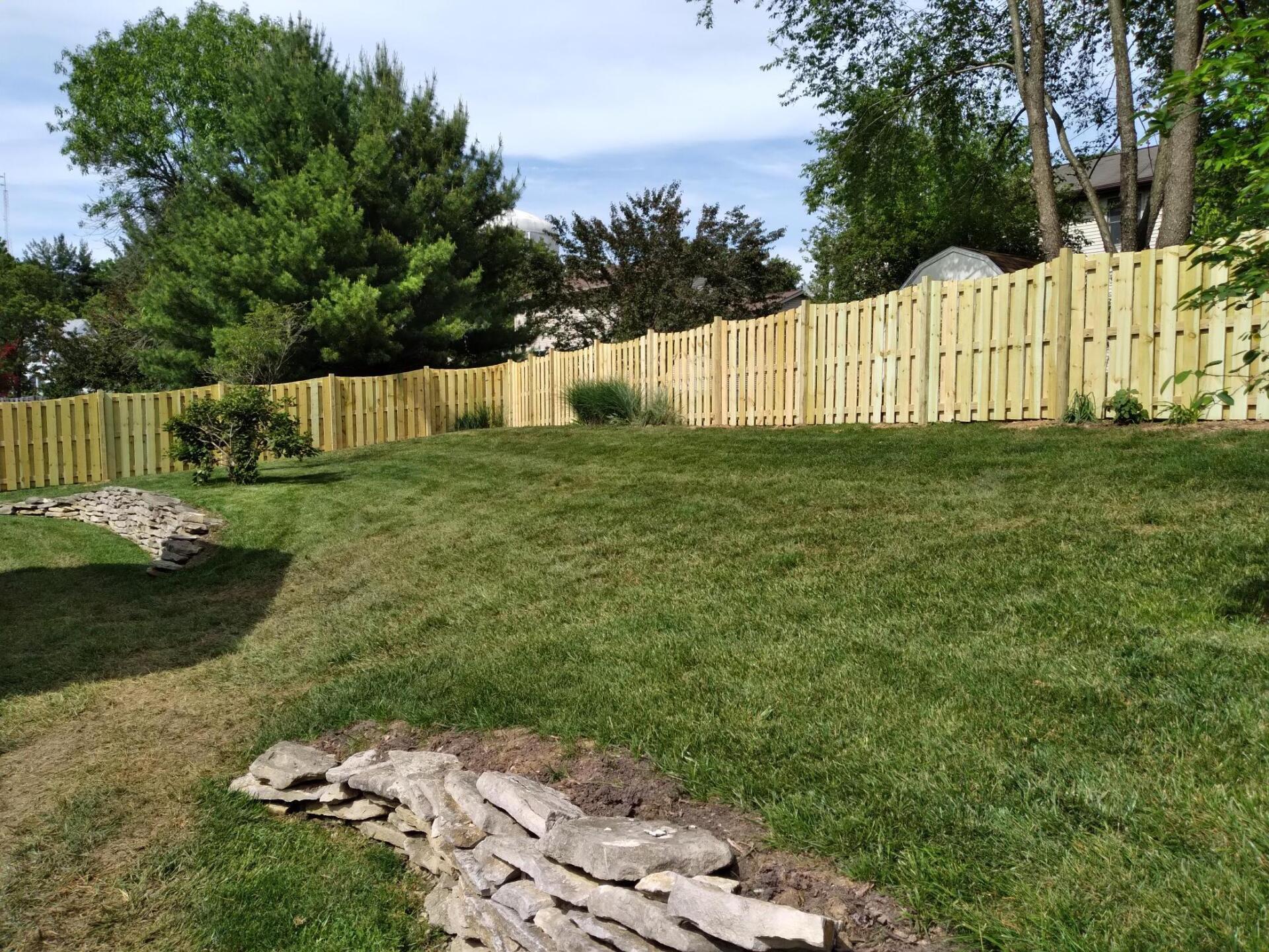 A wooden fence surrounds a lush green lawn in a backyard.
