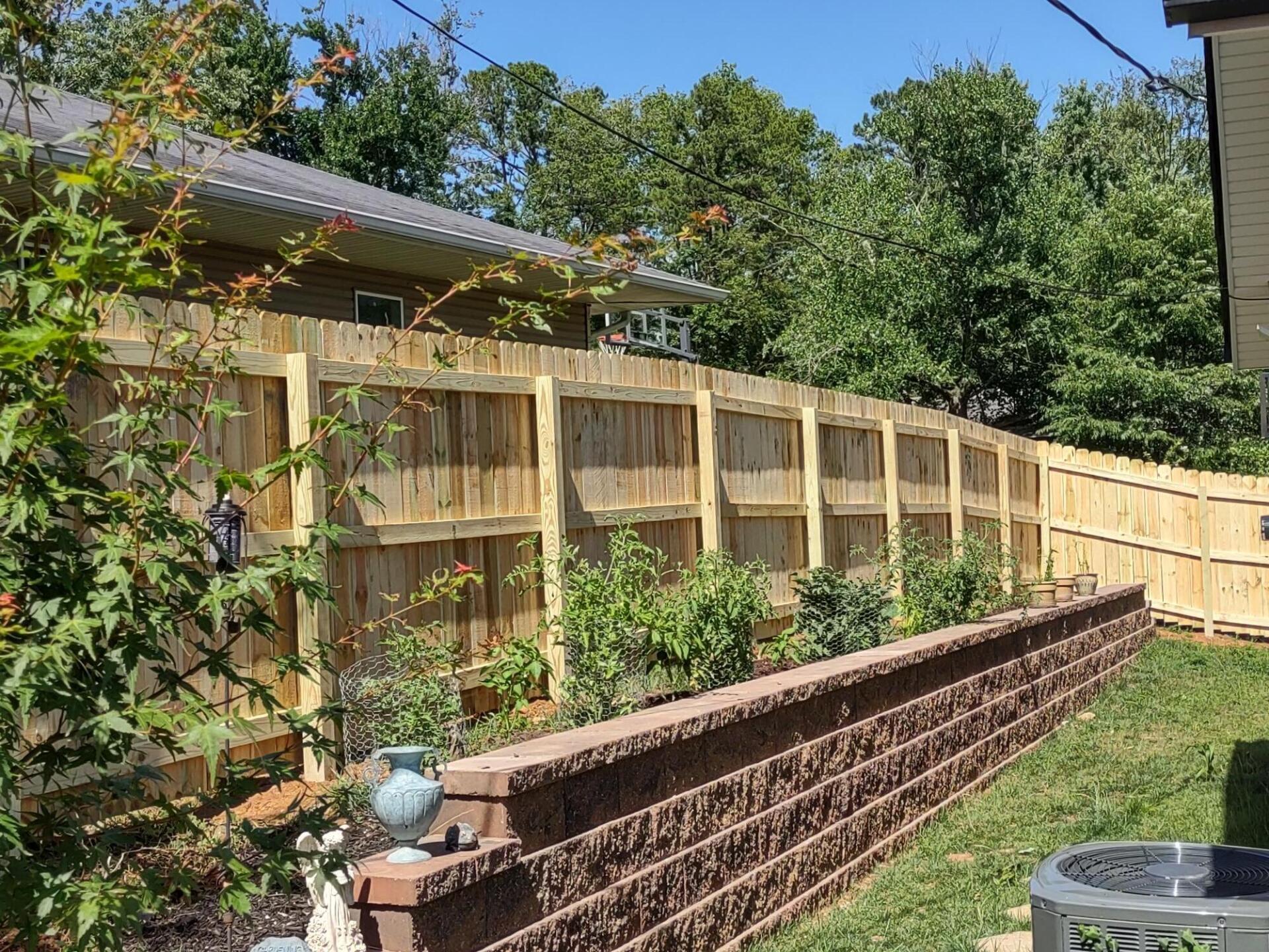 A wooden fence surrounds a brick wall in a backyard.