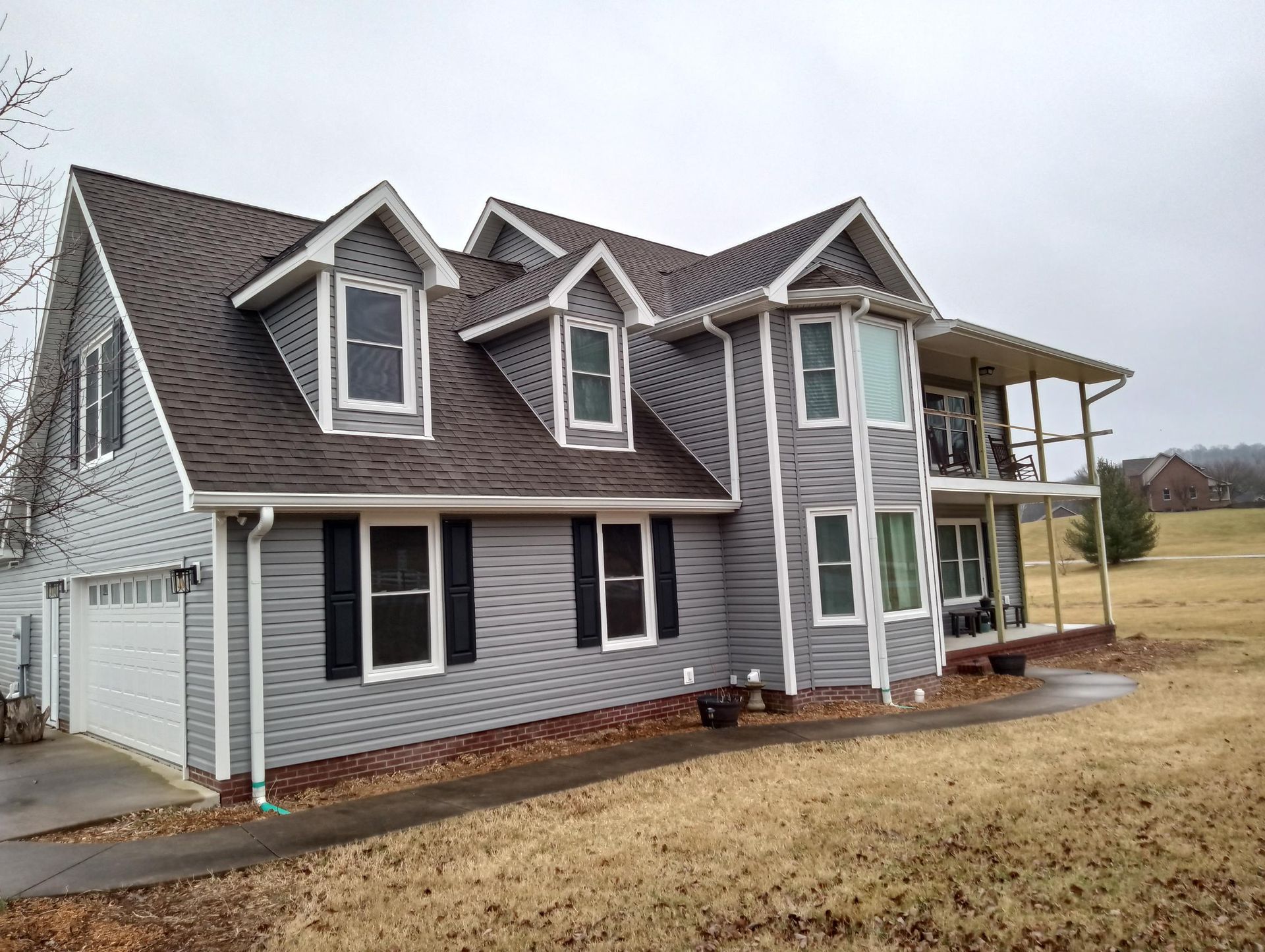 A large gray house with a brown roof is sitting on top of a grassy field.