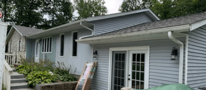 A large white house with a gray roof and a green umbrella in front of it.