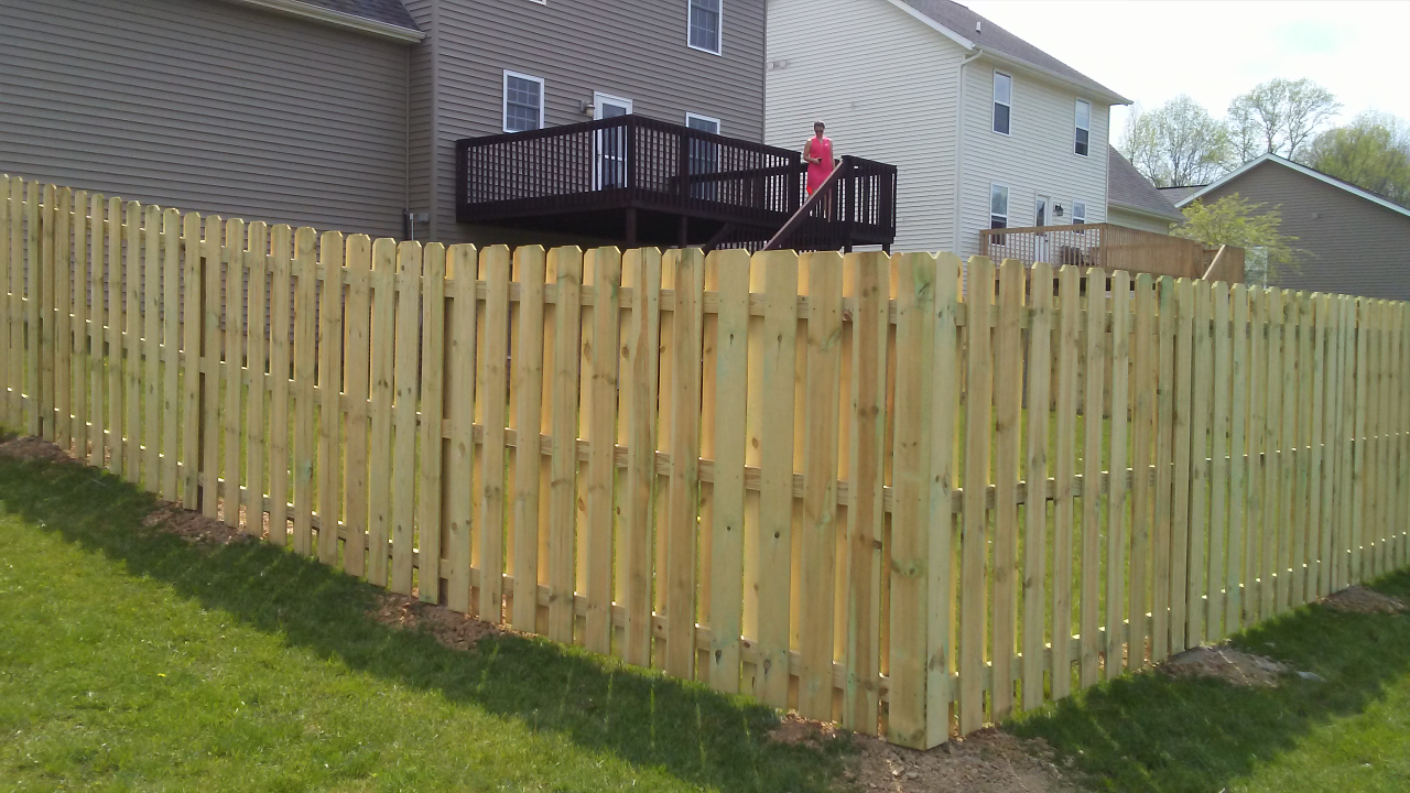 A wooden fence with a deck in the backyard of a house.
