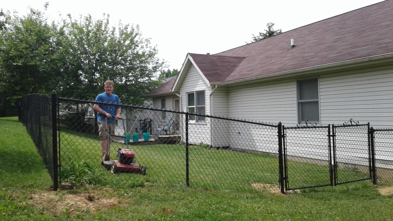A man is using a lawn mower to cut the grass in front of a house.