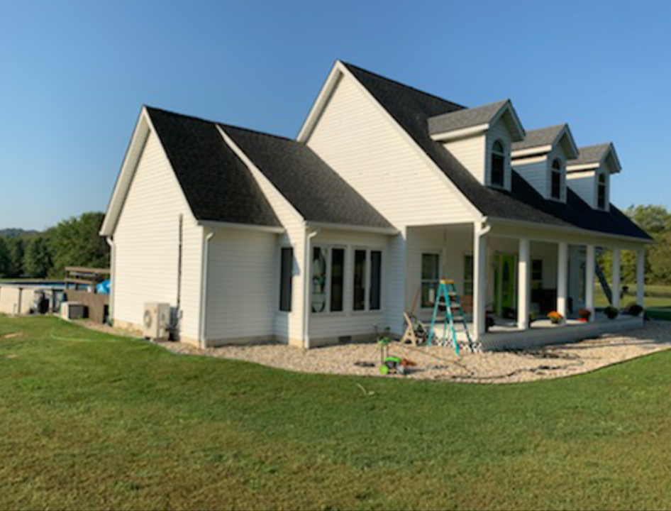 A large white house with a black roof is sitting on top of a lush green field.