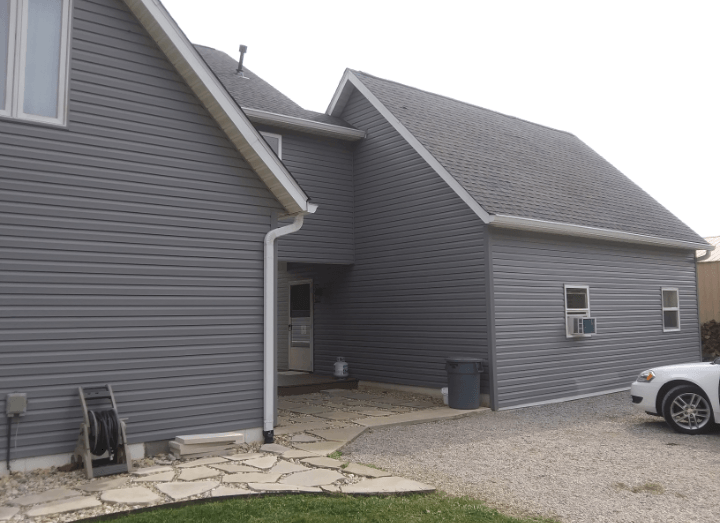 A white car is parked in front of a gray house