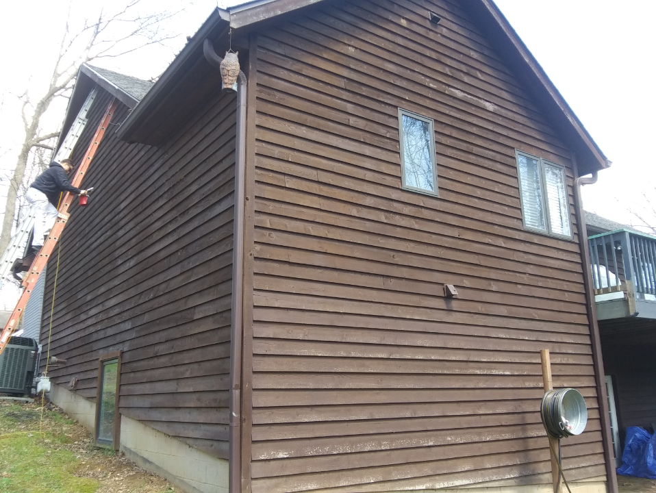 A man on a ladder is painting the side of a house