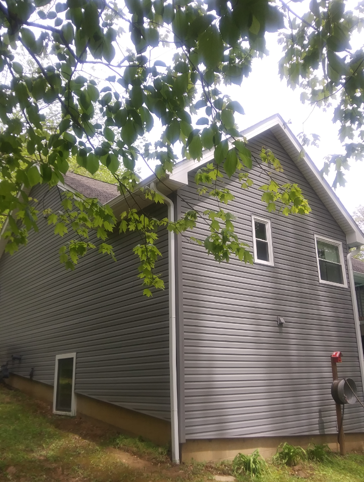 A house with a gray siding and white trim is surrounded by trees