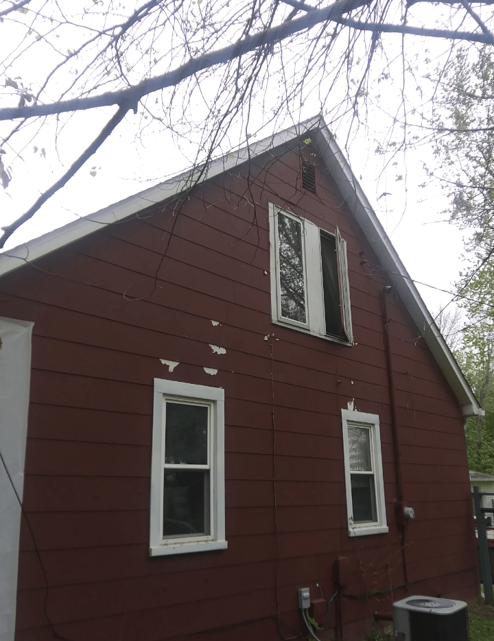A red house with white windows and a black air conditioner