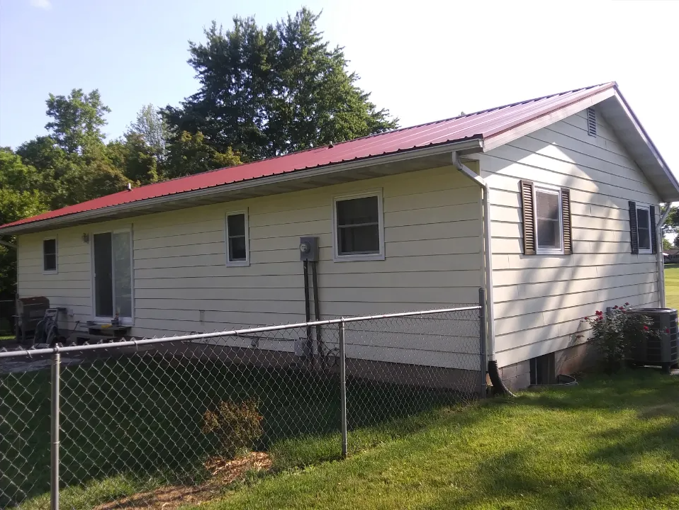 A white house with a red roof is behind a chain link fence