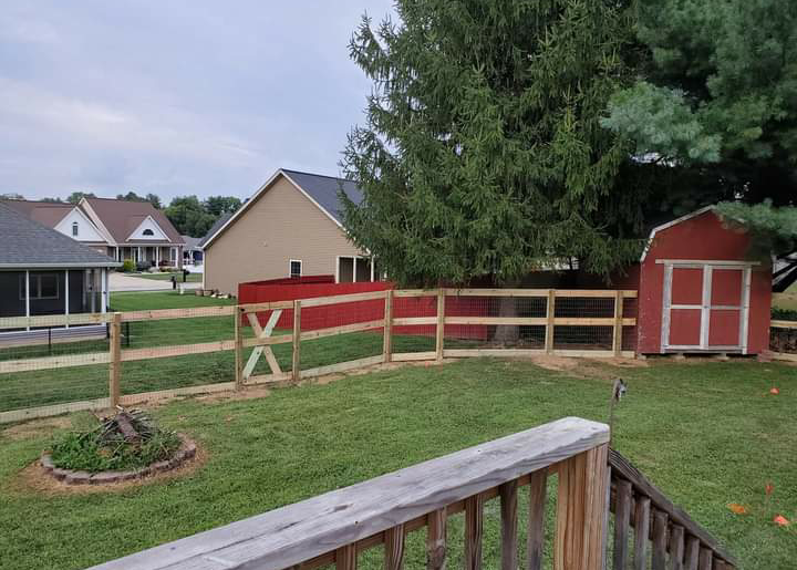 A wooden fence surrounds a yard with a red barn in the background.