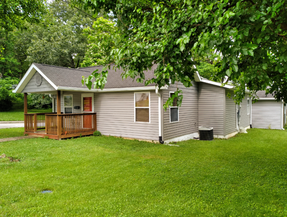 A small house with a porch and a garage is sitting on top of a lush green lawn.