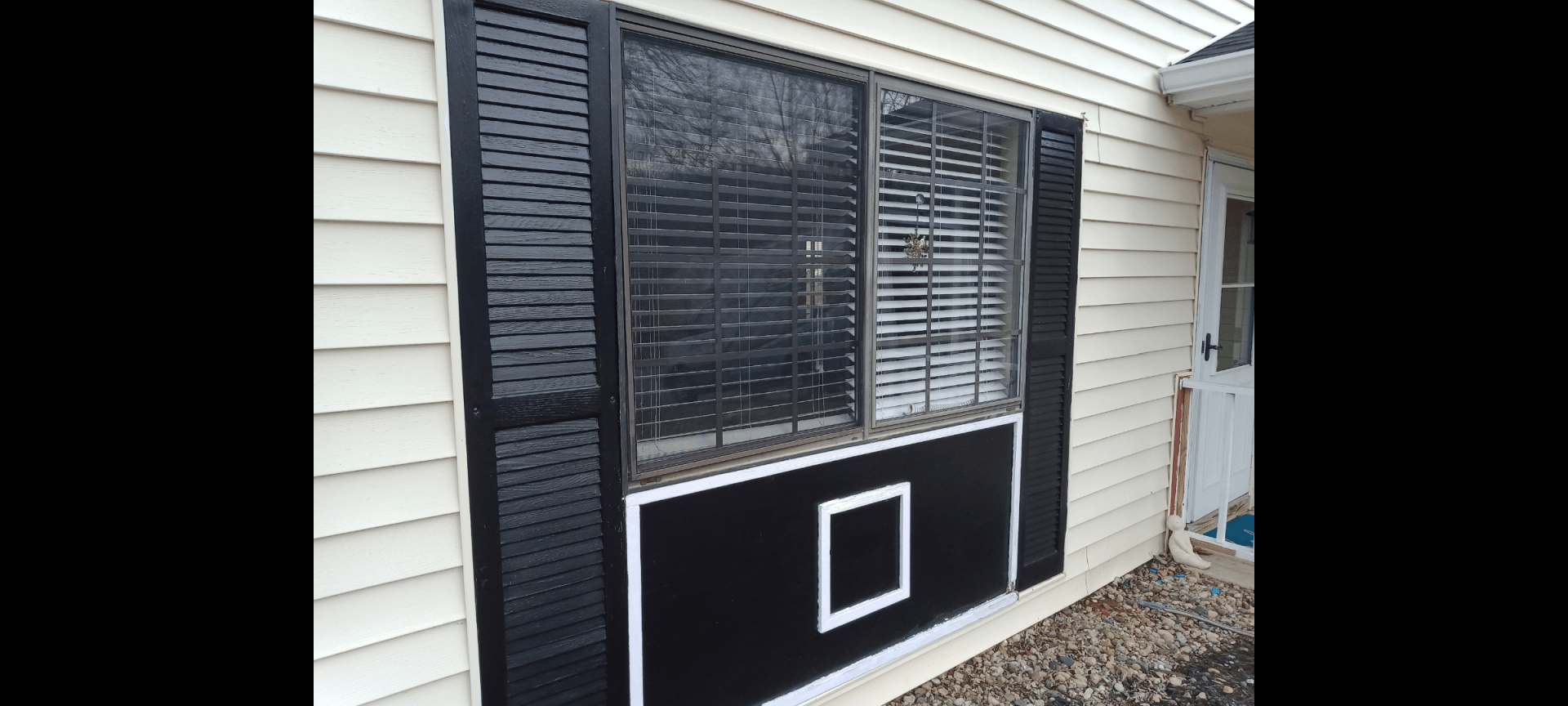 A window on the side of a house with black shutters.
