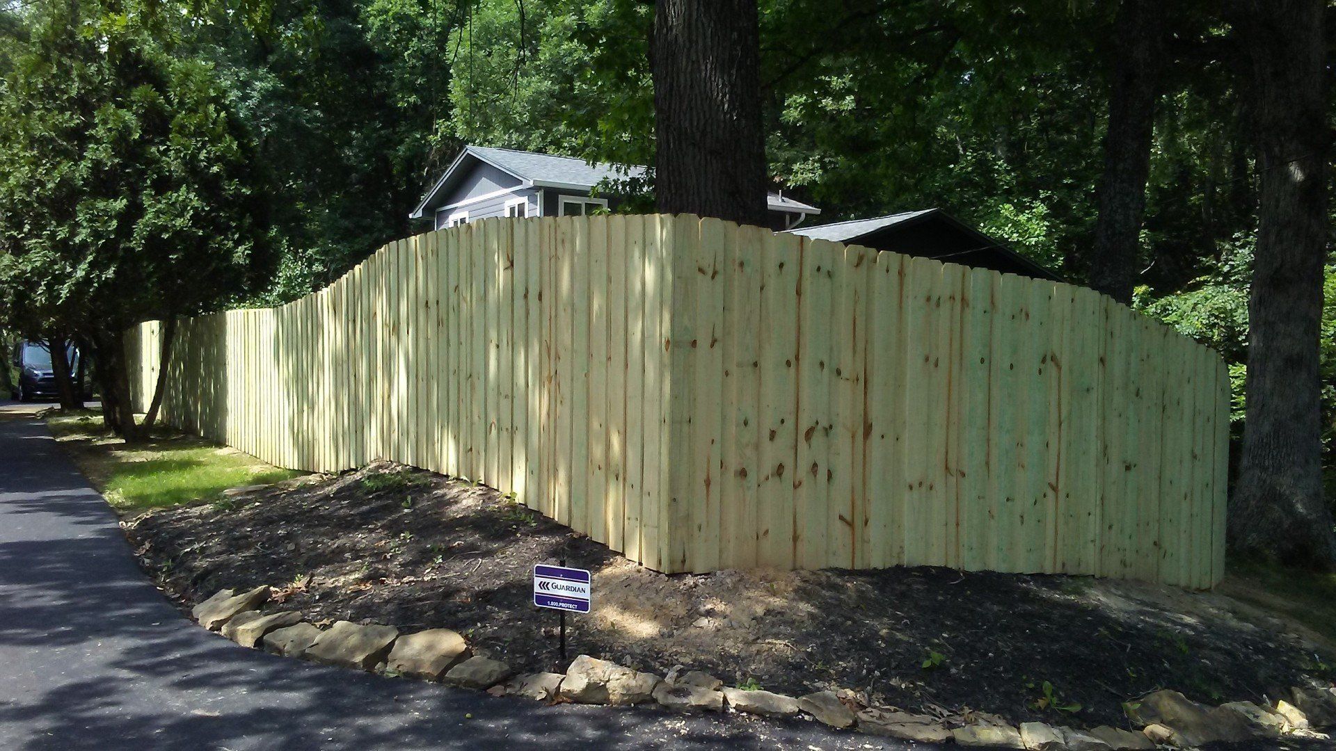 A wooden fence is surrounded by trees on the side of a road.