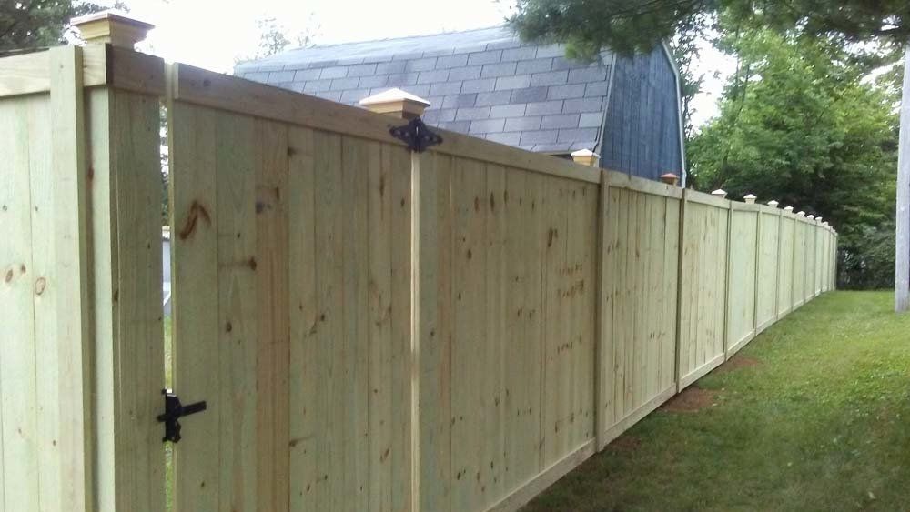 A wooden fence with a gate is surrounded by grass and trees.