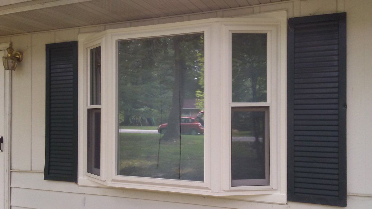 A white bay window with black shutters on a white house.