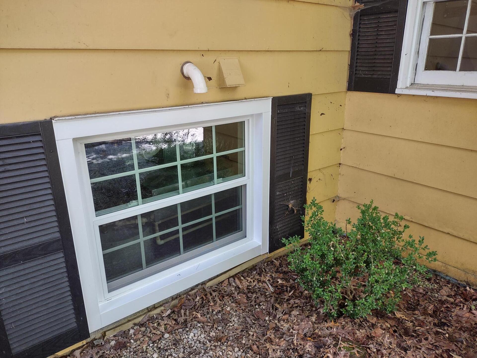 A window on the side of a yellow house with black shutters.