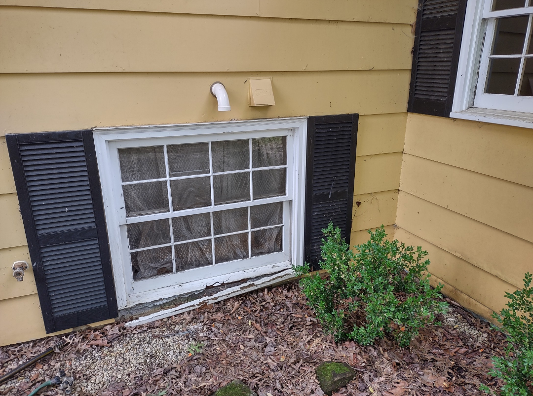 A window on the side of a yellow house with black shutters.