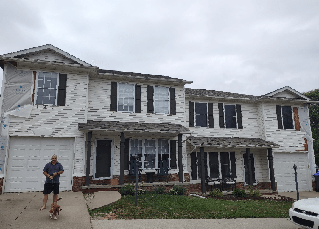 A man is walking a dog in front of a large white house.