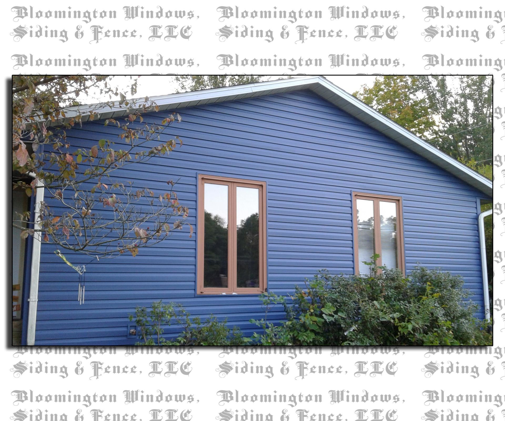 A blue house with brown windows is surrounded by trees and bushes.