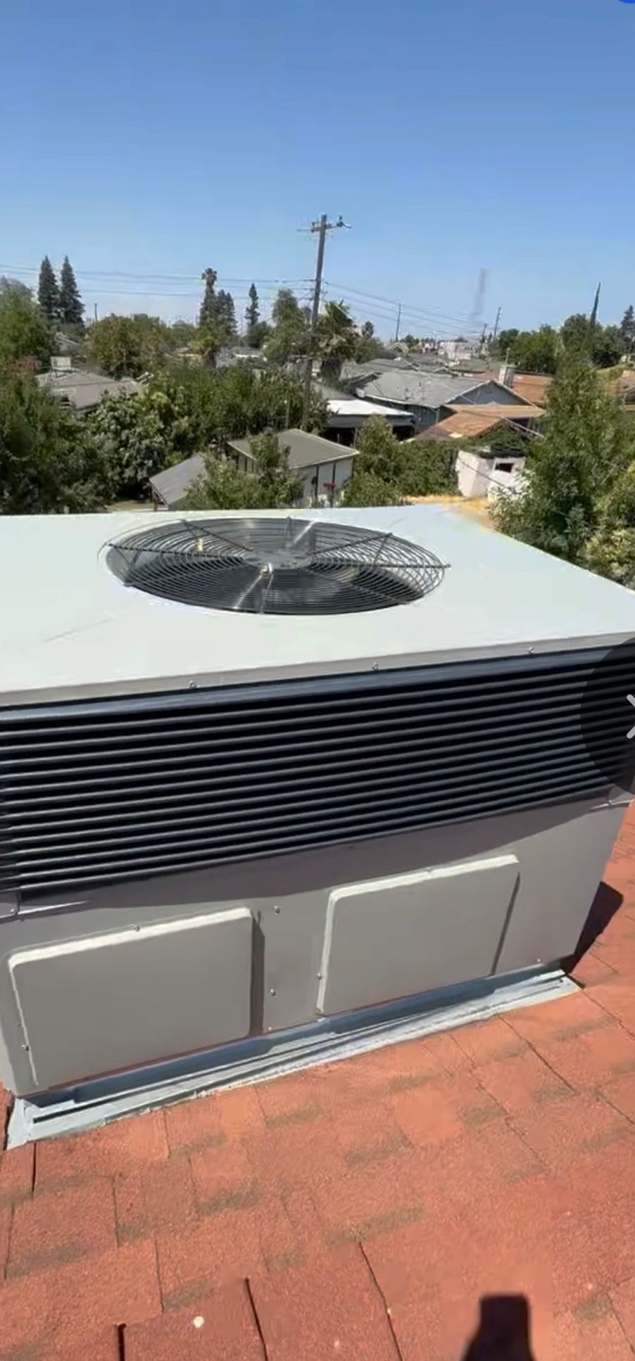 Outdoor HVAC unit on a rooftop with a circular fan top and gray vents, overlooking trees and houses
