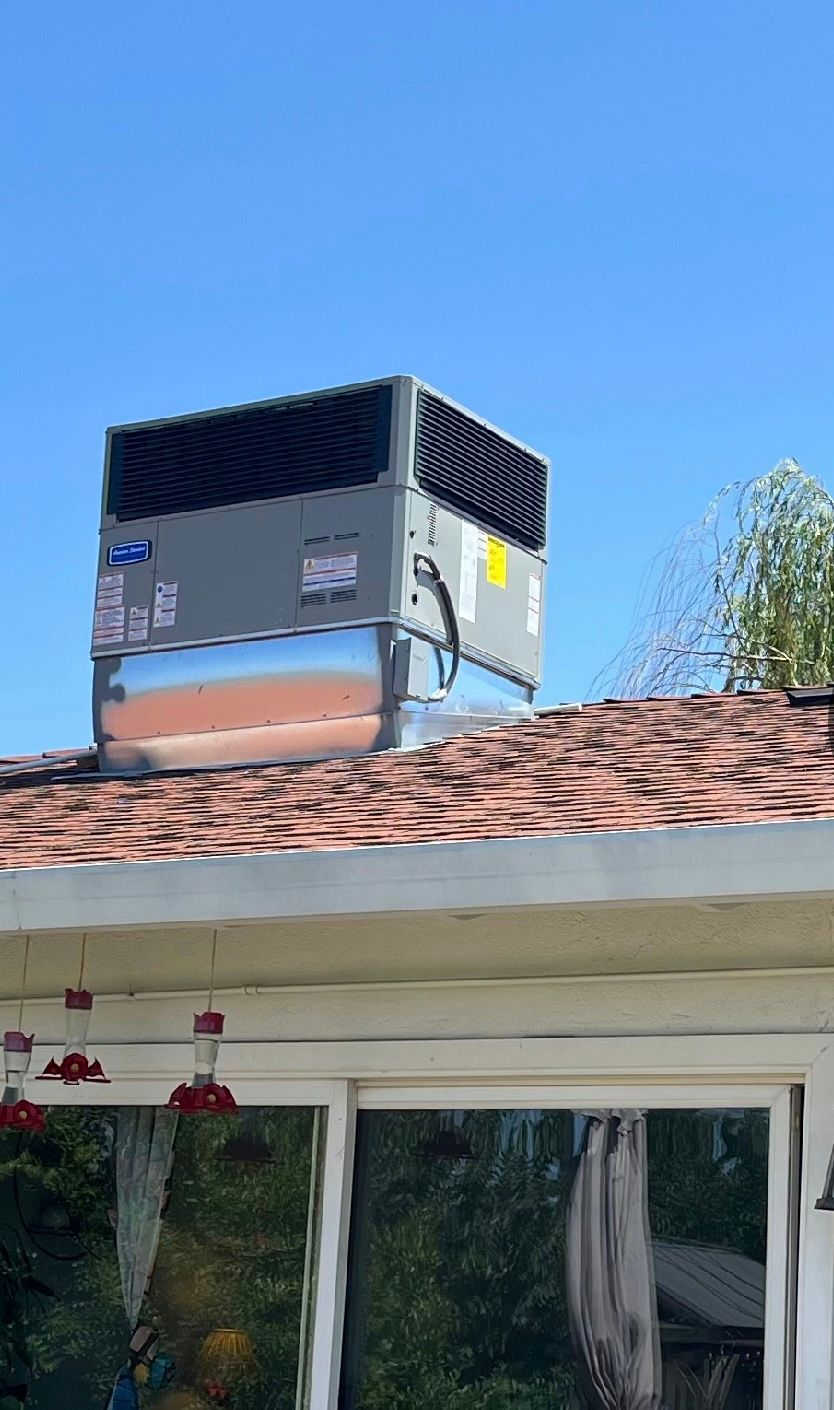 Large rooftop HVAC unit on a house with a shingled roof and white trim.