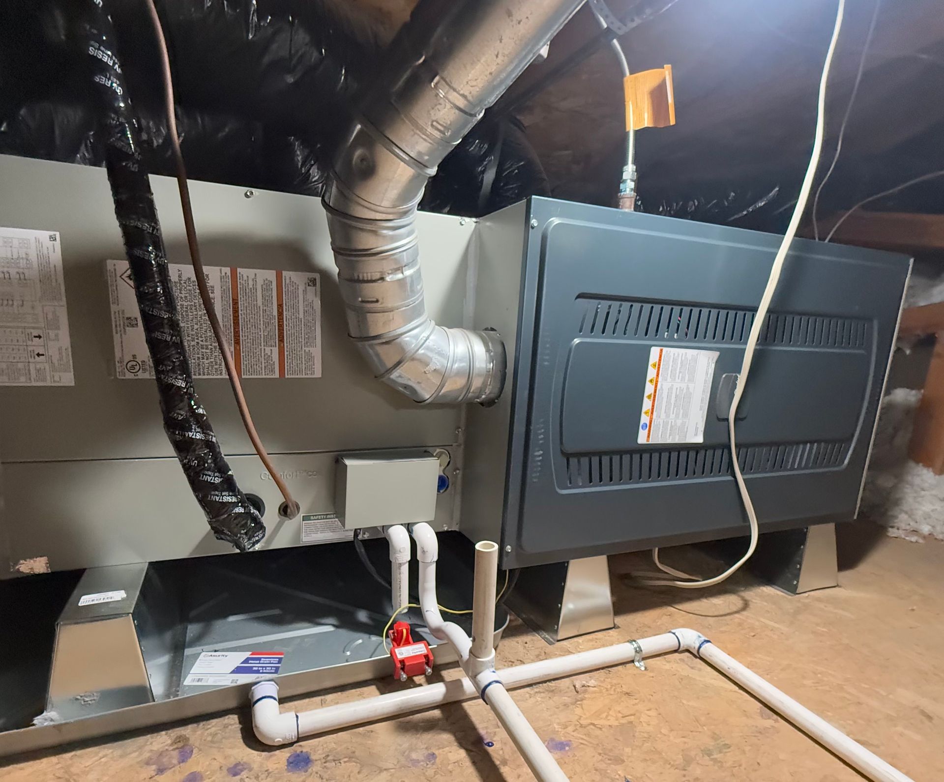 Basement HVAC furnace with ductwork, pipes, and a red valve on the floor.