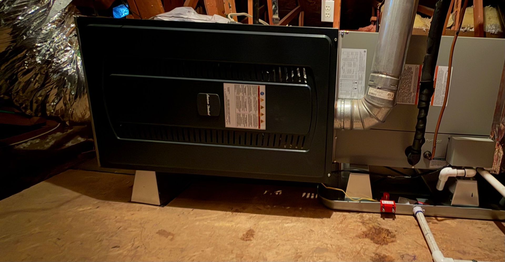 Black furnace or HVAC unit with metal ductwork in a basement or utility room.