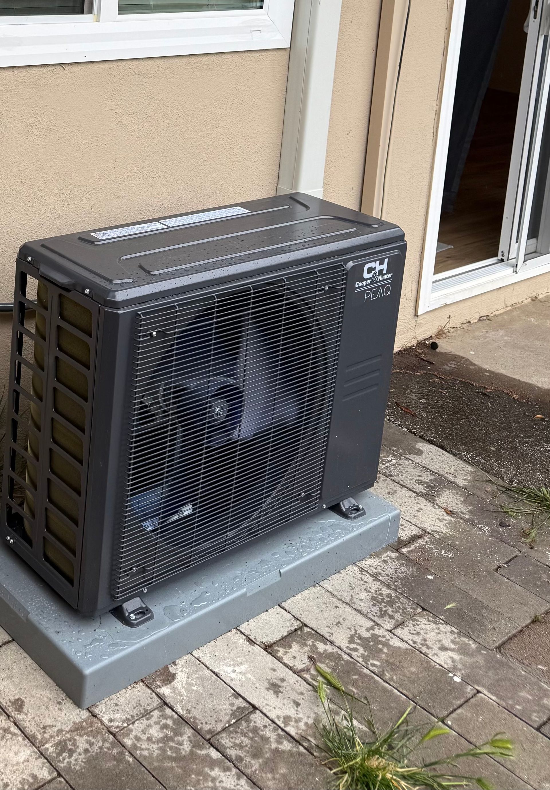 Outdoor air-conditioning unit beside a house doorway on a gray concrete pad