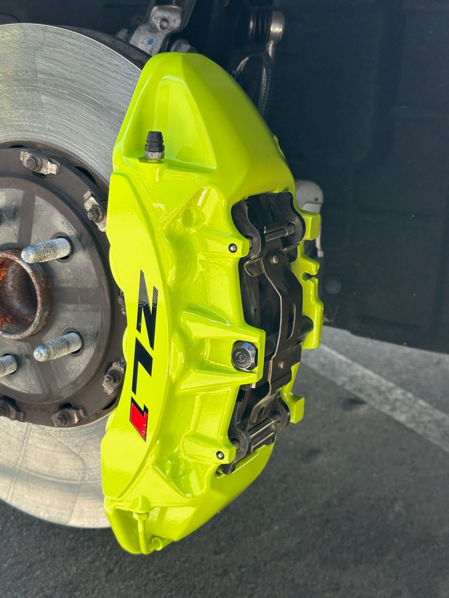 A man is sitting on a mat in front of a red car.