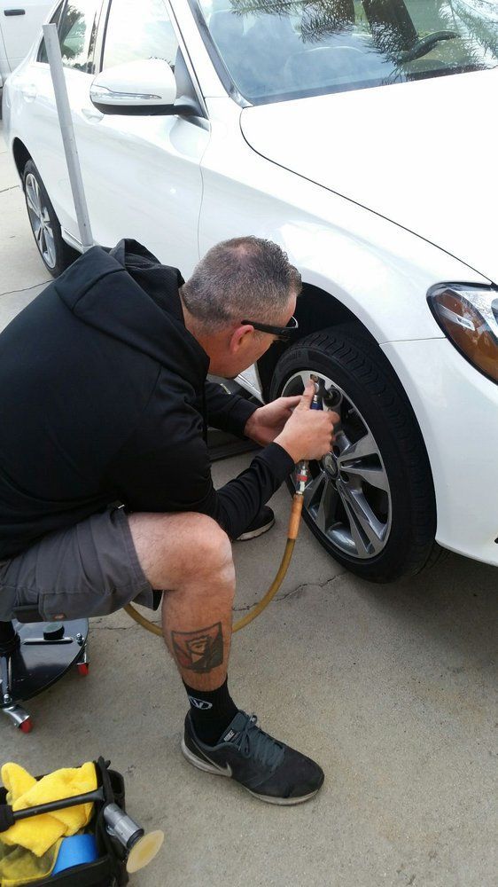 A man is inflating a tire on a white car.