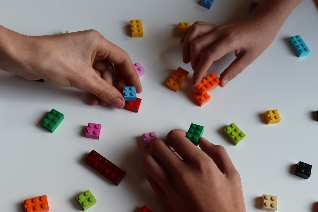 Een persoon en een kind spelen met legoblokjes op een tafel