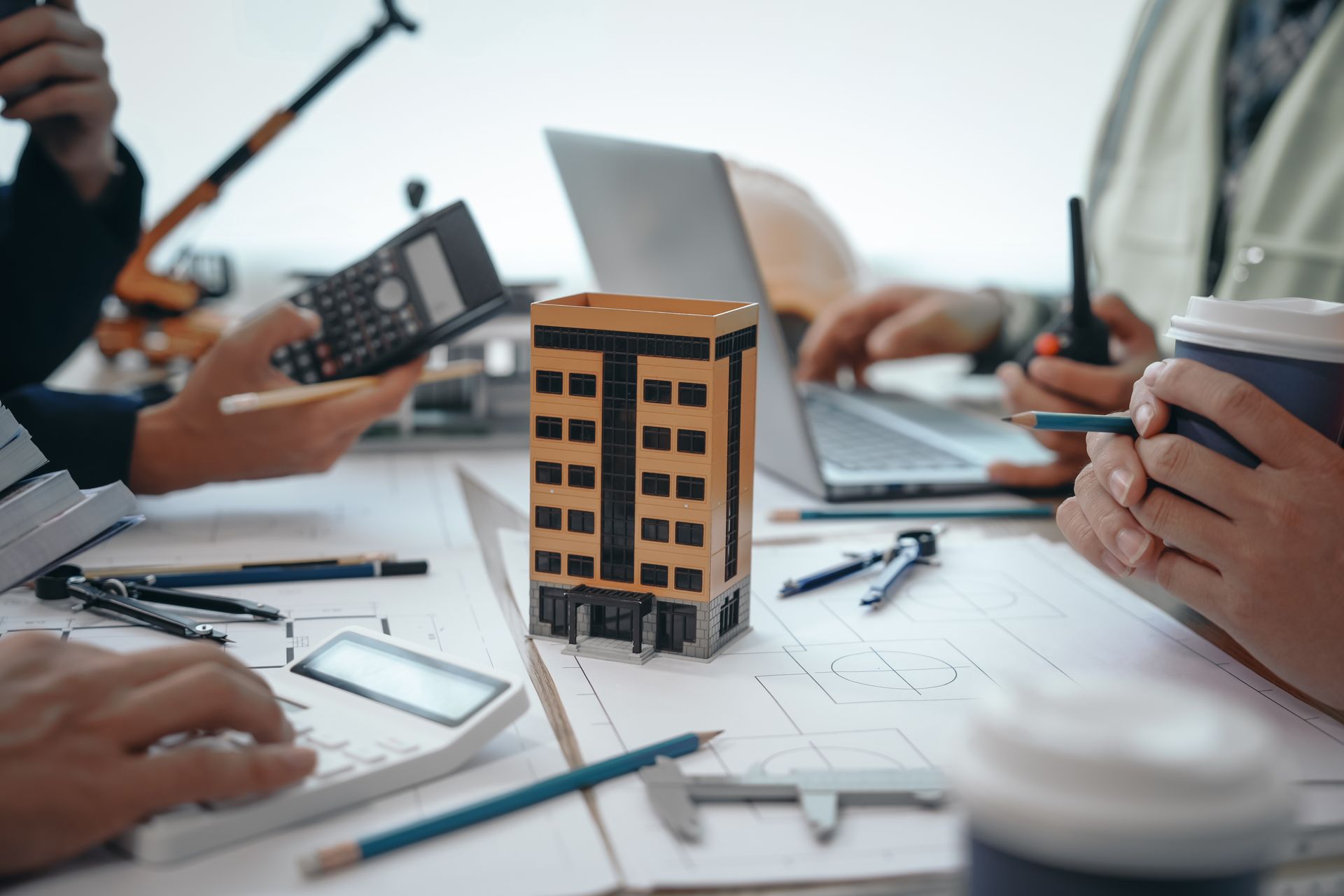 A group of people are sitting at a table with a model building and a calculator.