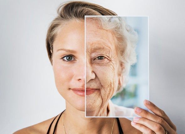 Young woman holding a transparent panel showing an aged version of her face; representing aging.