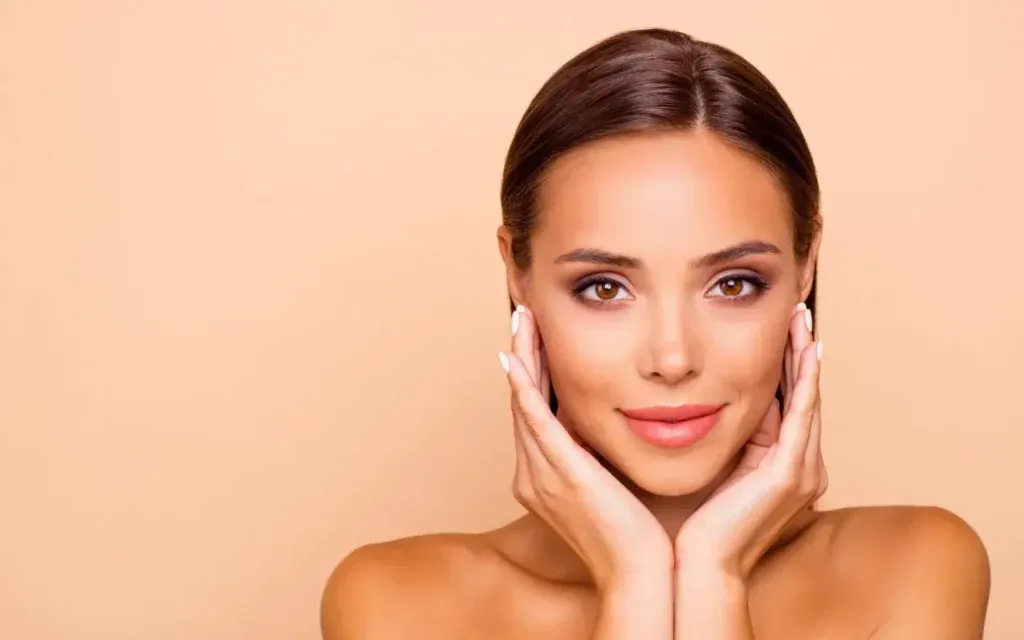 A Woman Is Touching Her Face with Her Hands and Smiling.