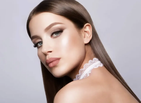 Woman with sleek, straight brown hair, wearing a white lace choker, and soft makeup, looking over her shoulder.