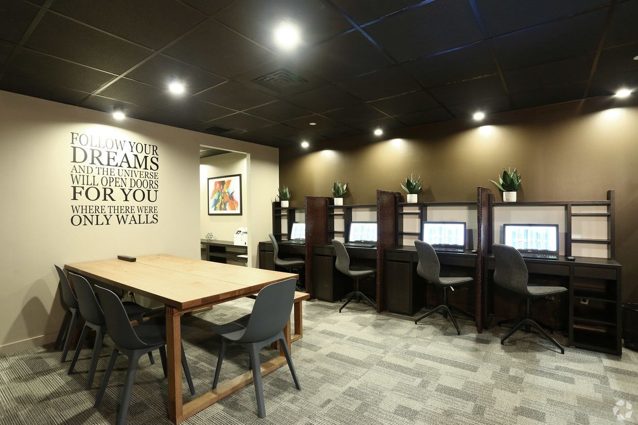 A room with a table and chairs and cubicles with computers.