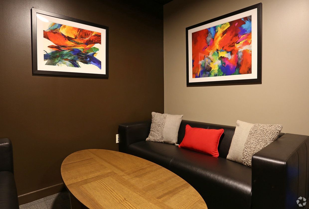 A living room with a couch , table , and two paintings on the wall.