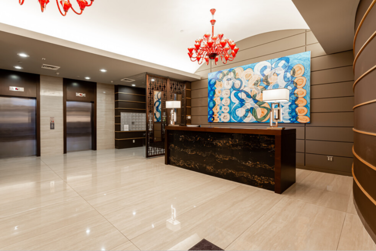 Lobby with marble floors, reception desk, abstract artwork, elevators, and a red chandelier.