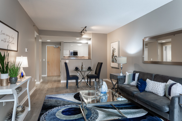 Modern living room with gray walls, dark gray sofa, blue rug, and small dining area.