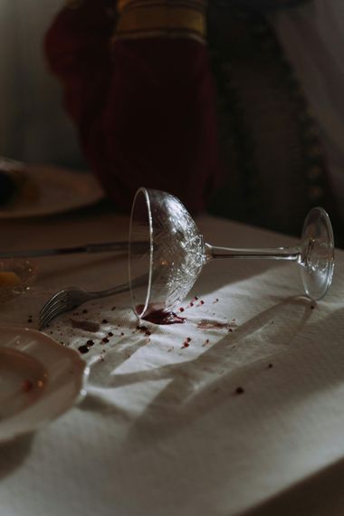 Broken wineglass on a table with spilled red wine and crumbs in dim light