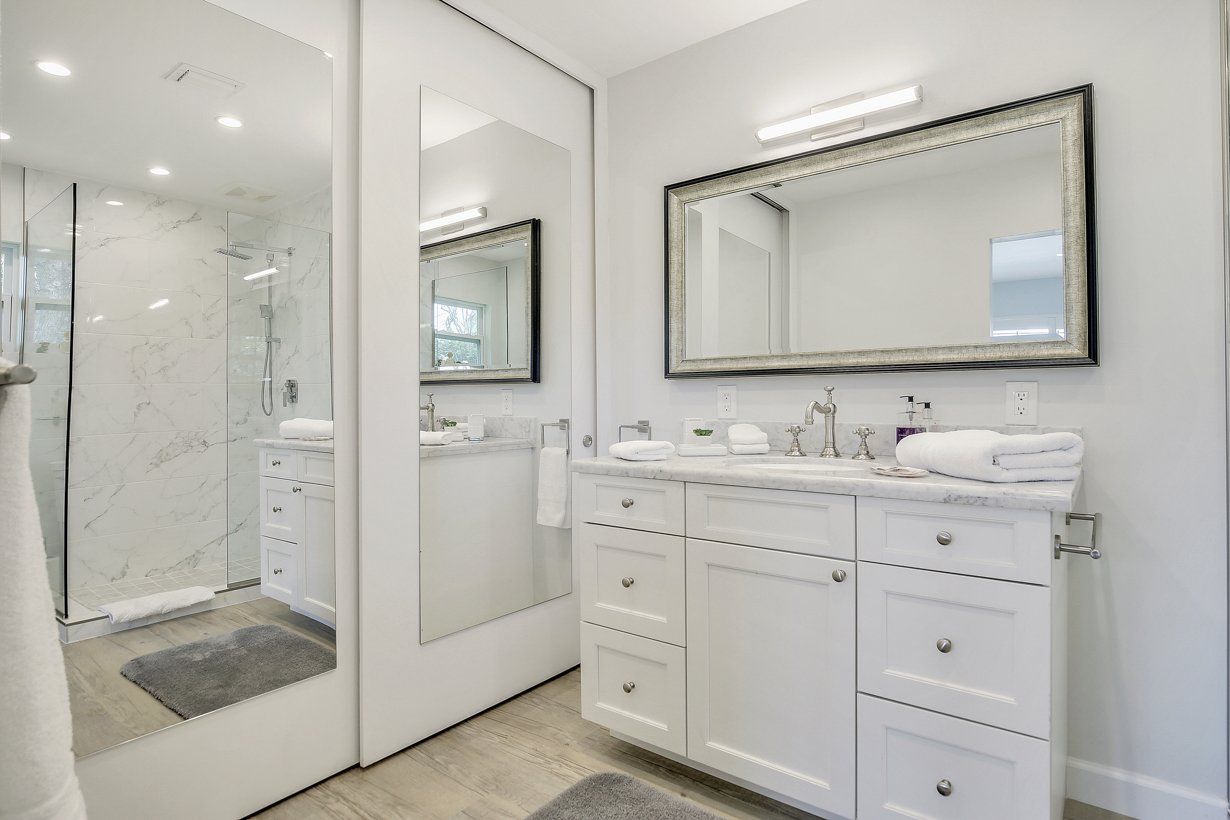 A bathroom with two sinks , two mirrors and a walk in shower.