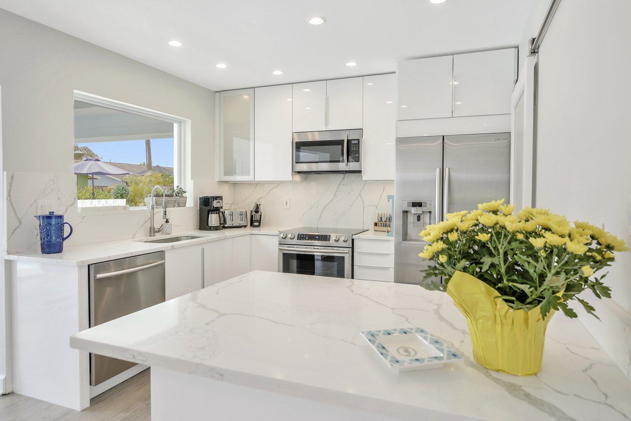 A kitchen with white cabinets and stainless steel appliances and a yellow vase of flowers on the counter.